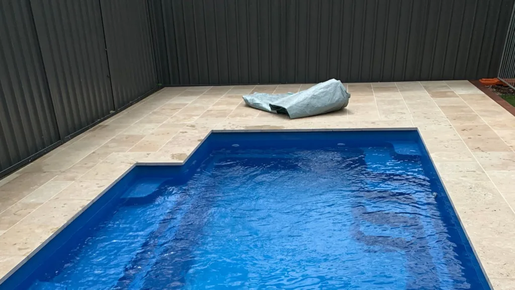 Small backyard pool with tiled deck and covered object