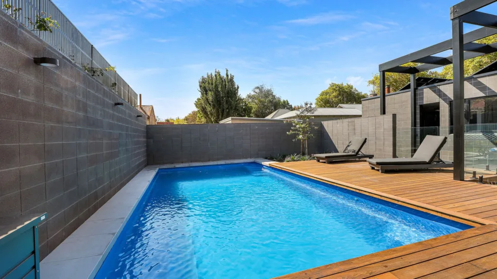 Modern backyard pool with wooden deck and lounge chairs